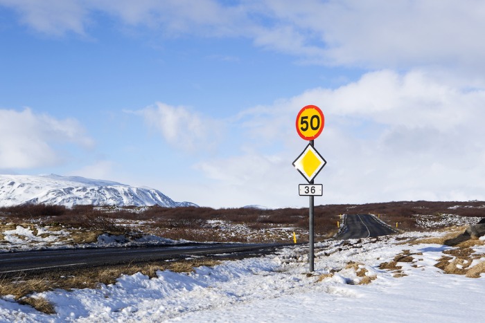 Una carretera islandesa completamente cubierta de nieve durante un día soleado y con una señal de tráfico amarilla que fija el límite de velocidad.