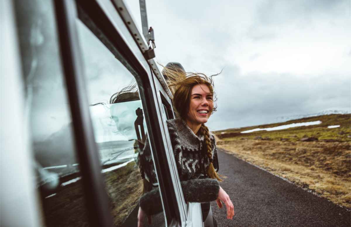 Consejos locales para conducir más seguro en Islandia Turista sacando la cabeza por la ventana de su camper de alquiler disfrutando de su viaje por Islandia