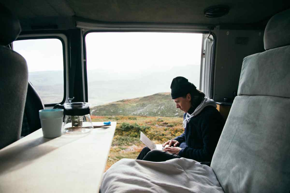 Viajero usando un port&aacute;til dentro de una camper con monta&ntilde;as islandesas al fondo.