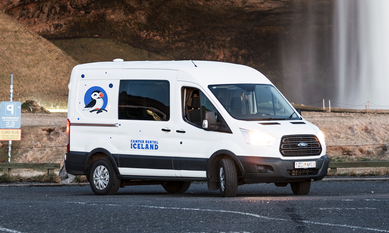 Camper Ford Transit estacionada junto a una cascada en Islandia