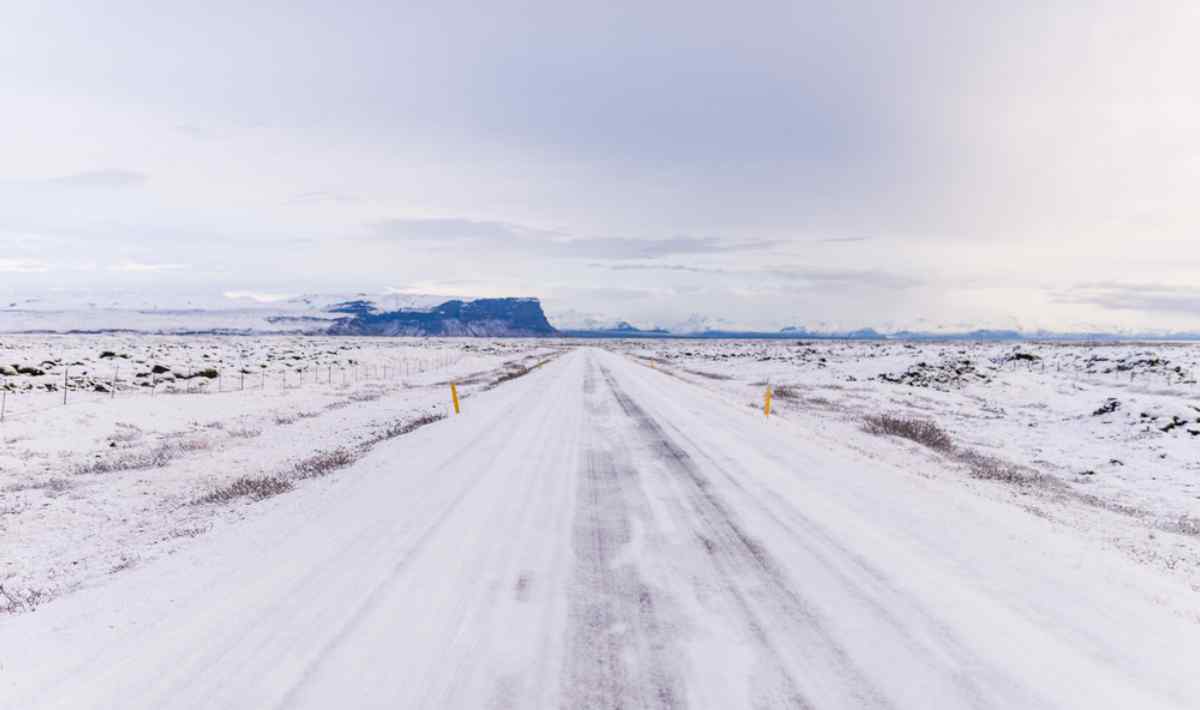 Carretera recta de Islandia cubierta de nieve y hielo bajo un cielo invernal p&aacute;lido.