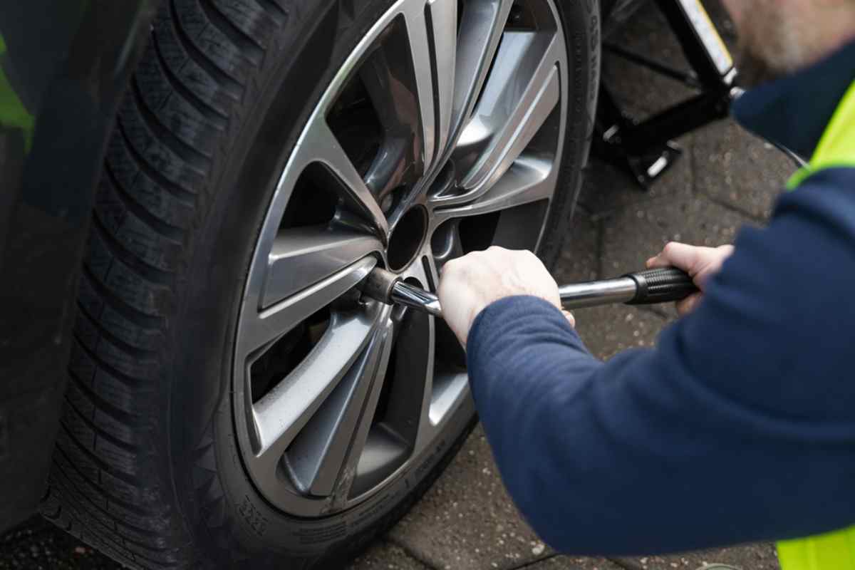Mec&aacute;nico apretando las tuercas mientras cambia una rueda de coche con tiempo fr&iacute;o.