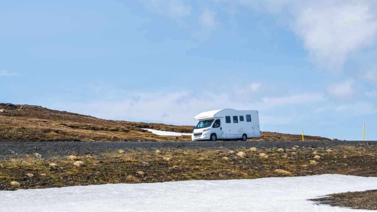 Autocaravana blanca que conduce por una carretera de monta&ntilde;a vac&iacute;a en Islandia con restos de nieve de final de primavera.
