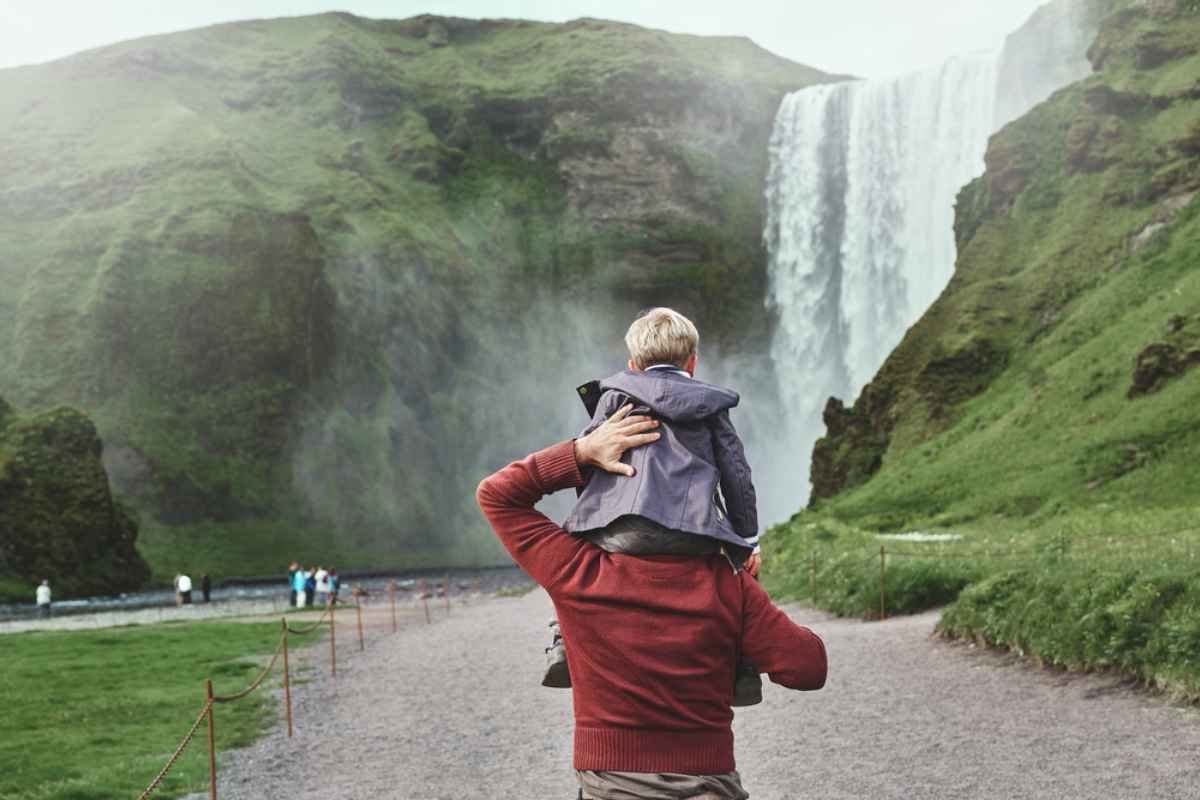 Persona adulta que lleva a un ni&ntilde;o sobre los hombros mientras caminan hacia la cascada Sk&oacute;gafoss en Islandia.