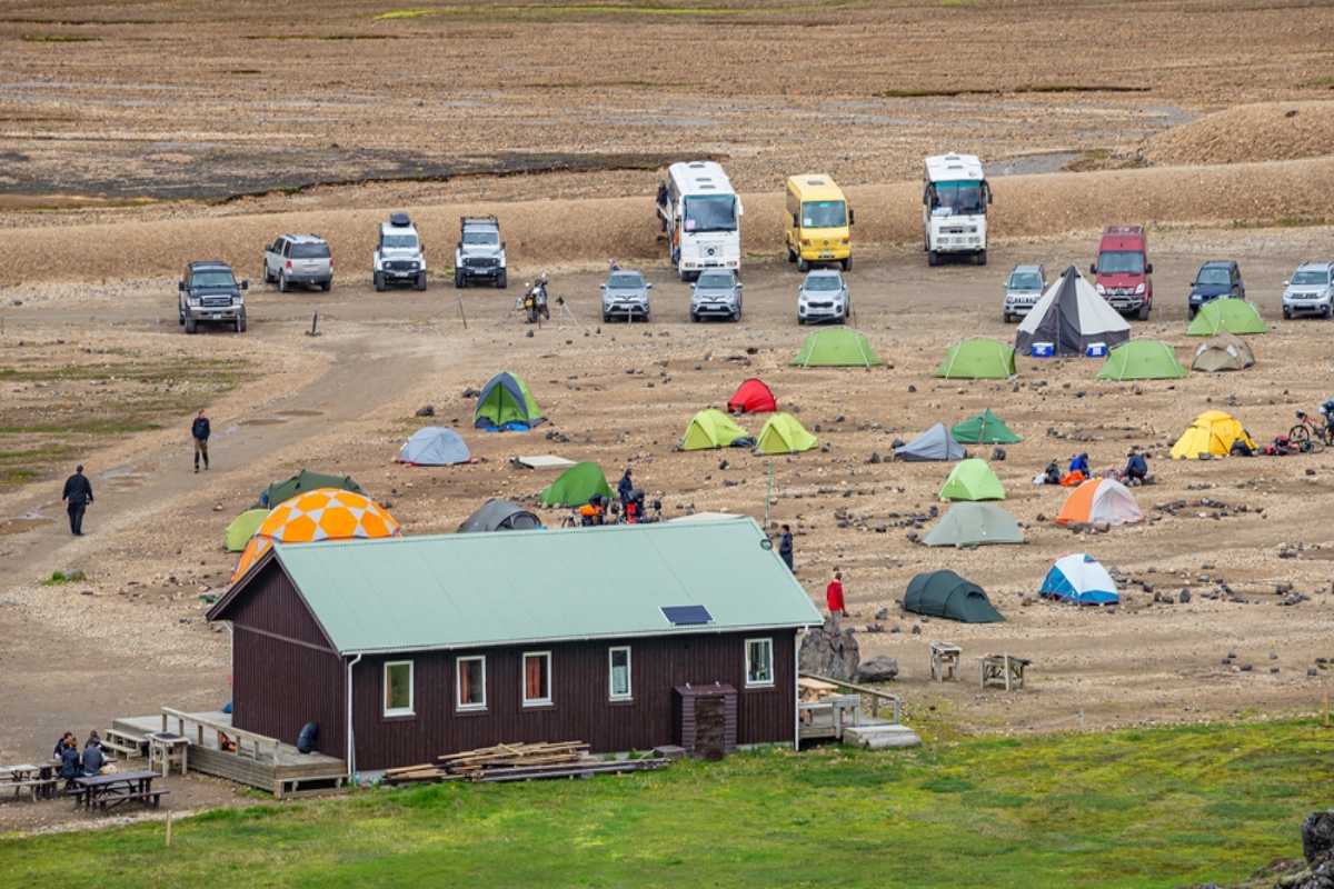 Acampar en Islandia con una autocaravana Camping concurrido en Islandia con tiendas de colores, vehículos aparcados y un pequeño edificio de servicios en un paisaje rocoso