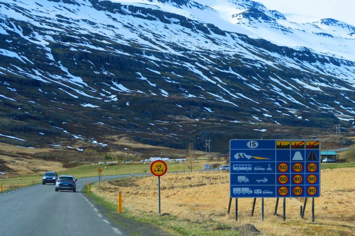 Límites de velocidad en Islandia Señal de carretera en Islandia que muestra los límites de velocidad nacionales junto a una carretera rural con montañas nevadas al fondo