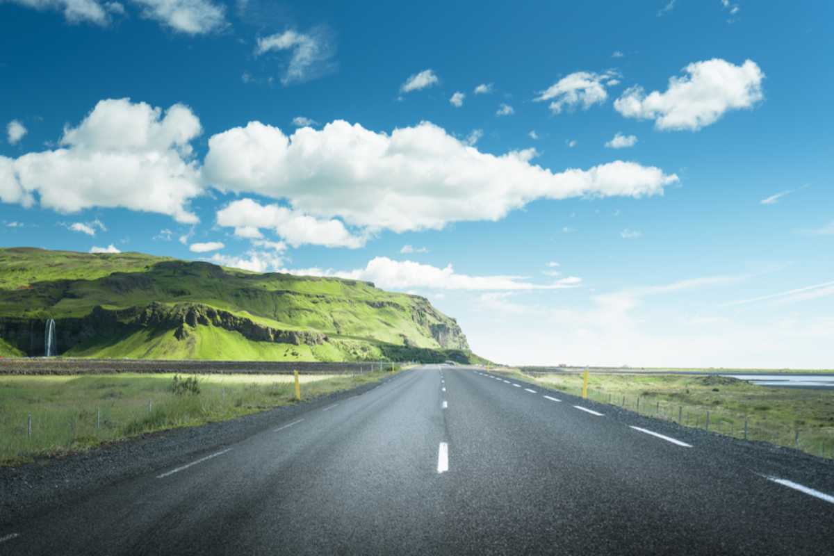 Verano en Islandia Carretera asfaltada vacía que atraviesa la Costa Sur de Islandia con acantilados verdes, campos abiertos y un cielo azul brillante