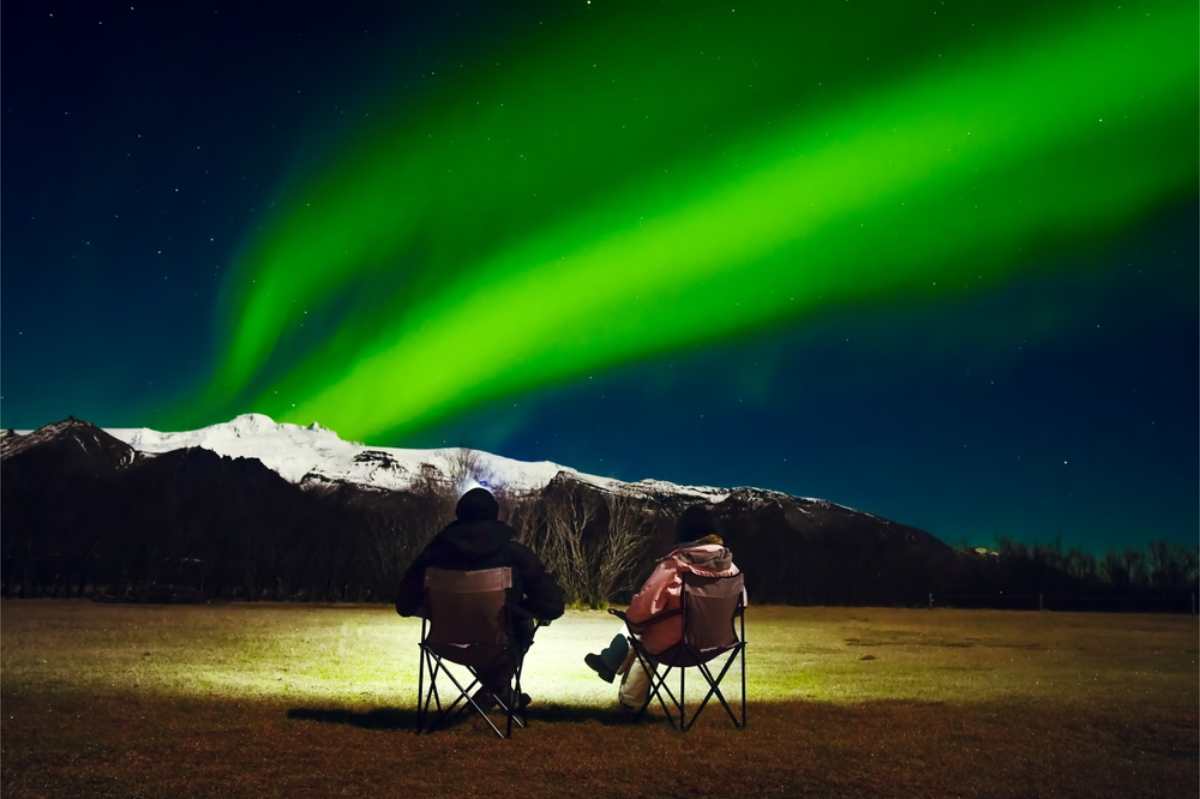 Dónde acampar en la Ring Road Turista sentado en su silla de camping bajo las auroras boreales