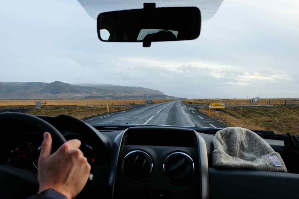Ring Road de Islandia Vista desde el interior de un coche conduciendo por una carretera asfaltada a través del campo abierto islandés.