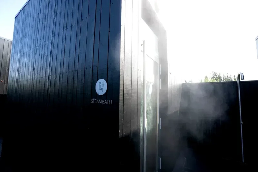 Serenidad Nocturna en Krauma Spa Geotérmico - Un Lugar de Relajación Perfecto en Islandia Piscina de spa geotermal en Krauma en Islandia, reflejando la suave luz nocturna con arquitectura moderna, rodeada de vegetación natural y banderas ondeando al viento.