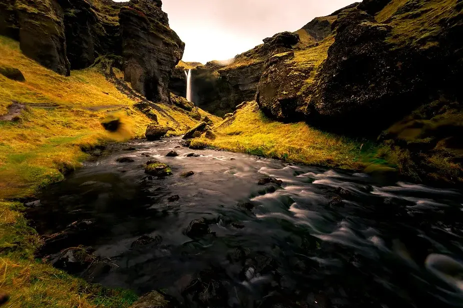 Vista serena de la catarata Kvernufoss rodeada de acantilados cubiertos de musgo con un arroyo que fluye en primer plano.