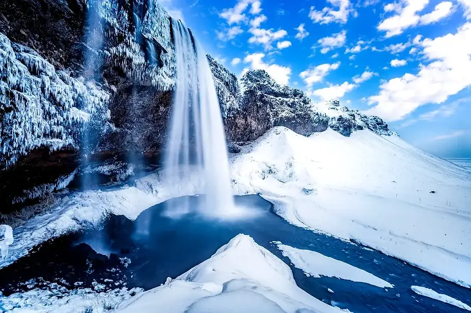 Cascada Seljalandsfoss en Islandia durante el invierno, rodeada de acantilados nevados y un paisaje congelado.