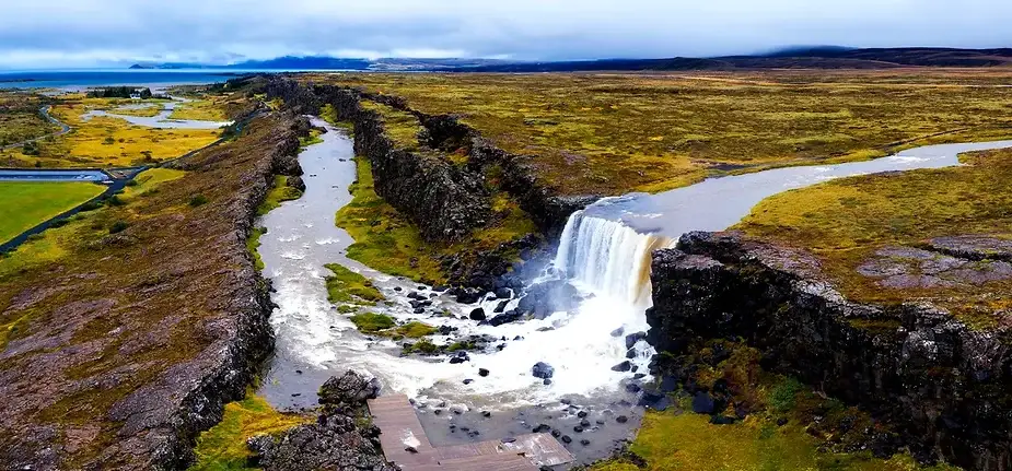 Vista aérea de la Cascada Öxarárfoss y el Valle de Rift Perspectiva aérea de la Cascada Öxarárfoss cayendo desde los acantilados hacia el valle de rift, con ríos y praderas rodeando la cascada en el Parque Nacional Thingvellir, Islandia.