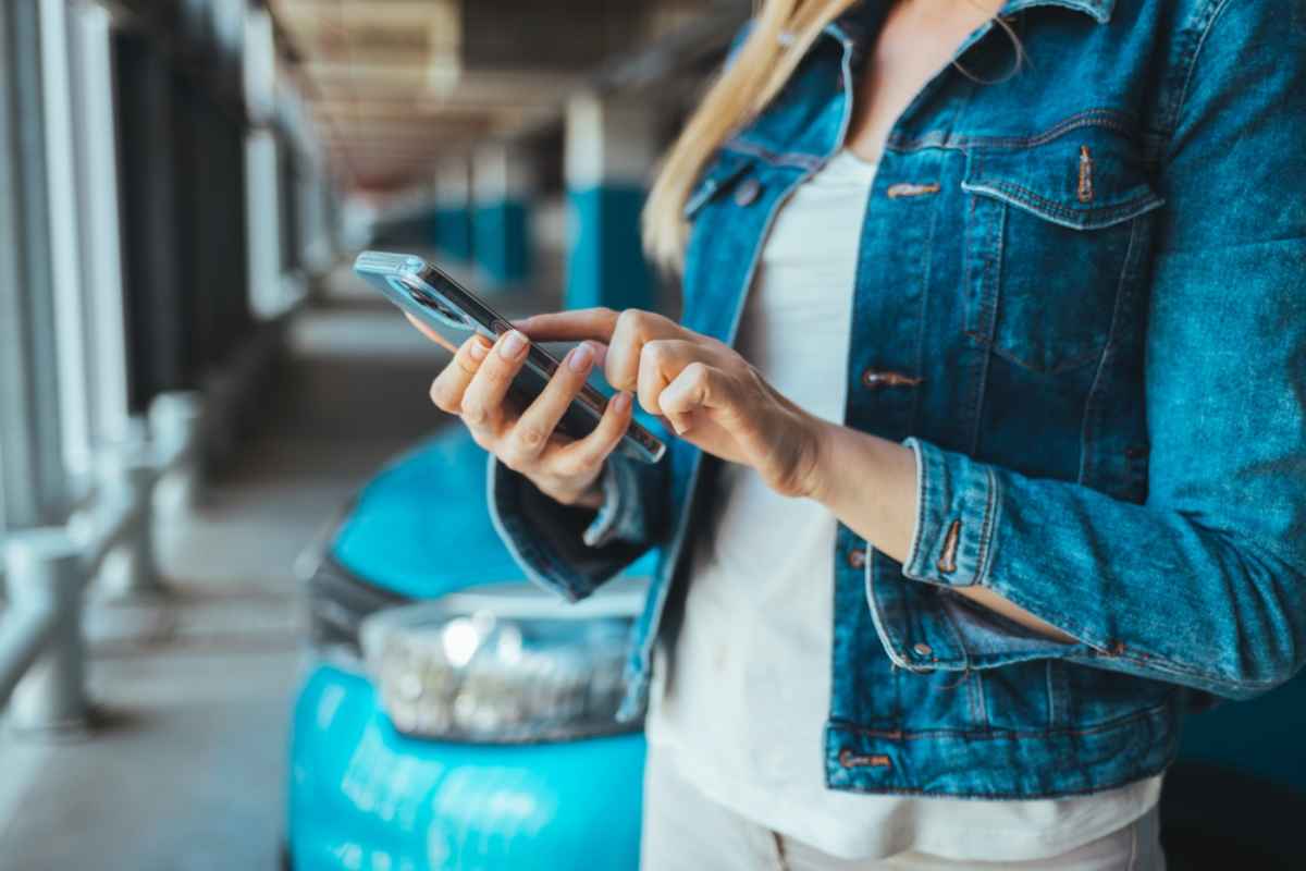 Une femme en veste en jean consulte son téléphone portable après avoir garé son véhicule dans un parking.