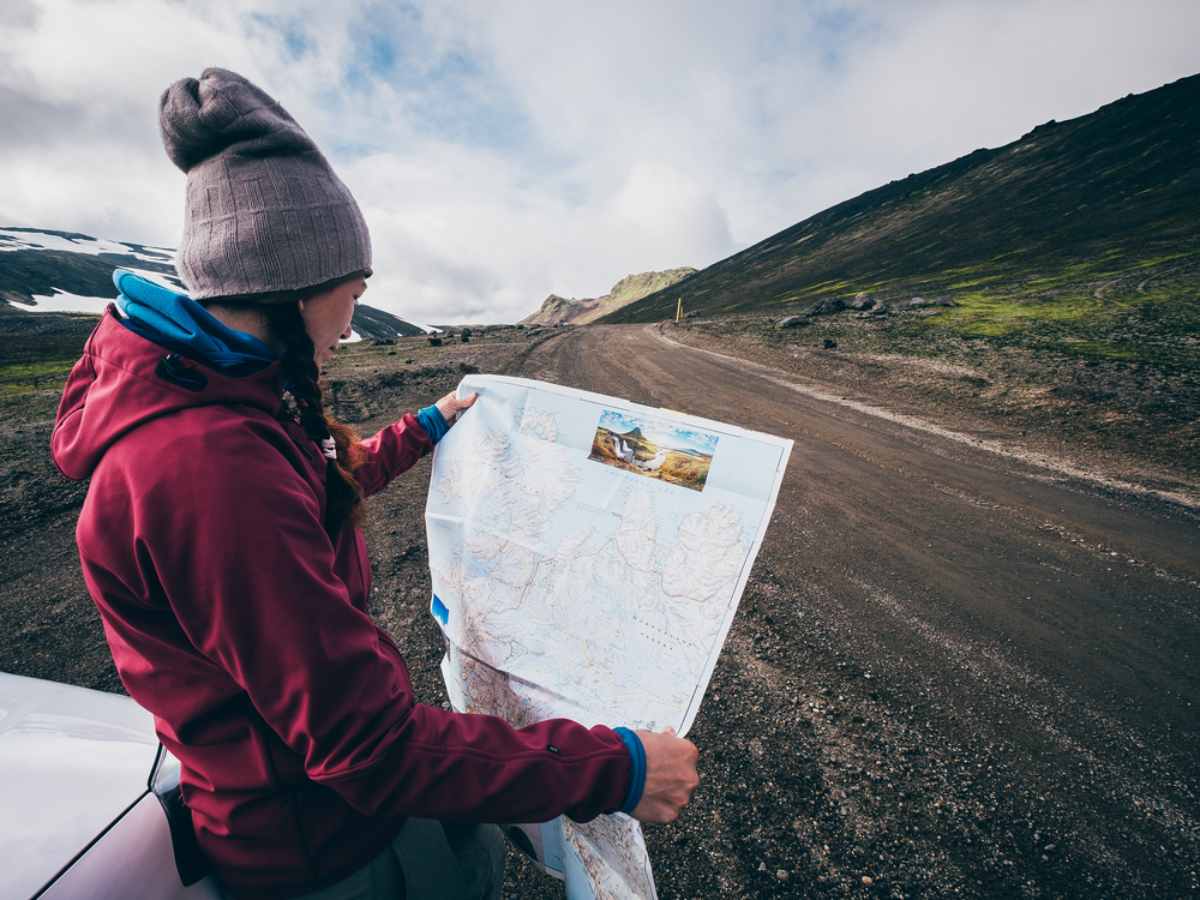 Touriste tenant une carte papier pr&egrave;s d&rsquo;une route de gravier en Islande