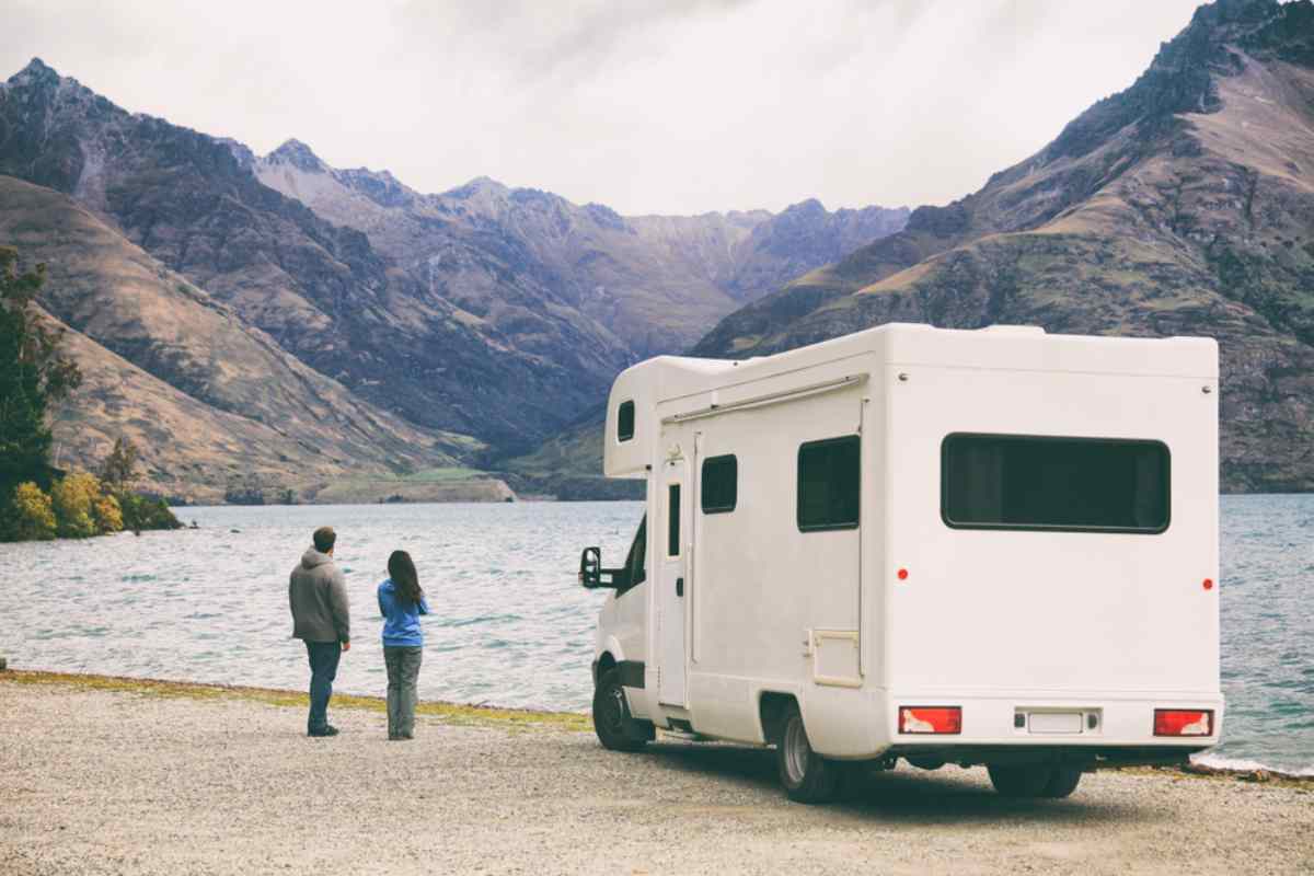 Couple debout à côté d’un camping‑car surplombant un lac et des montagnes.