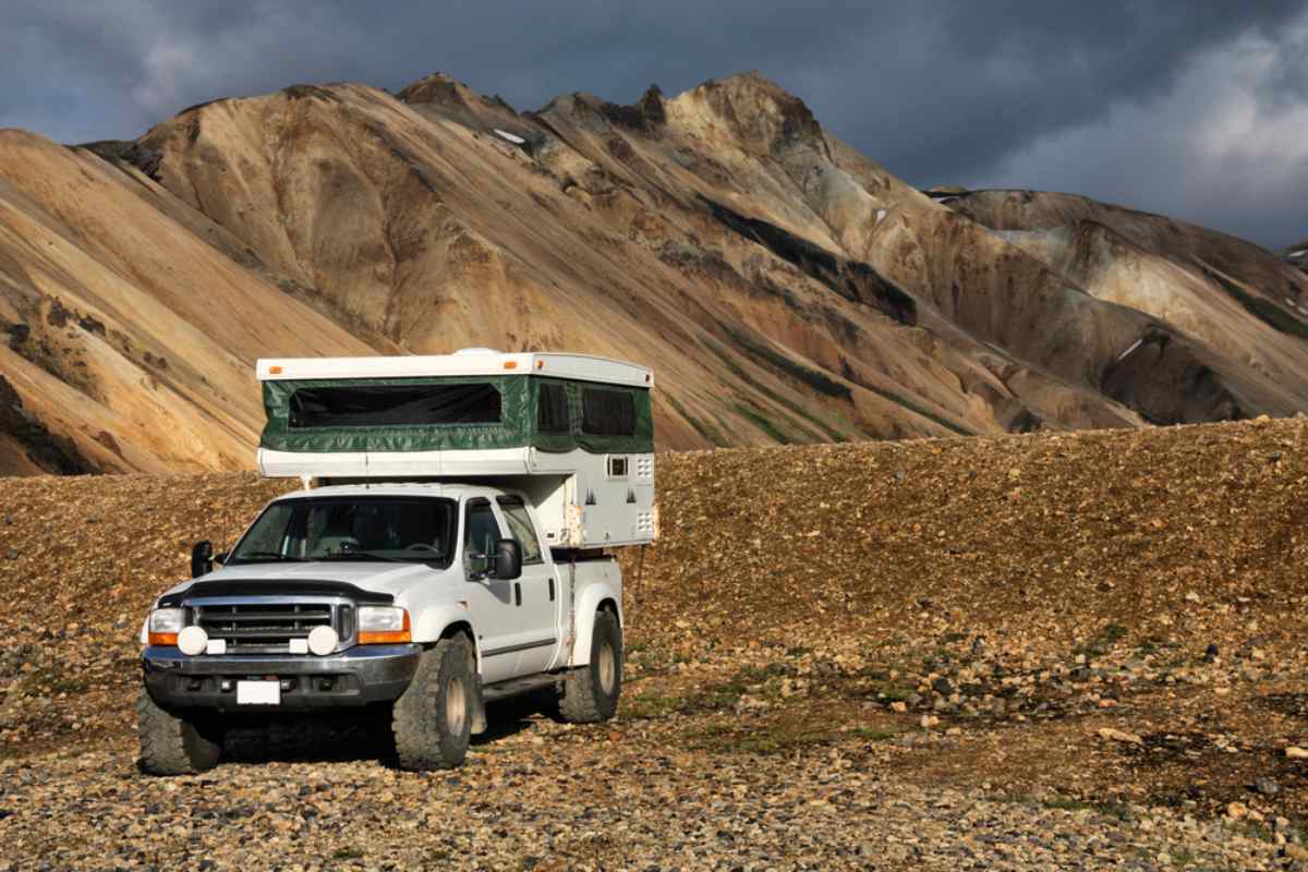 Quelle voiture louer en Islande ? Camping-car 4x4 sur pickup garé dans les Hautes Terres islandaises sous des sommets en rhyolite.