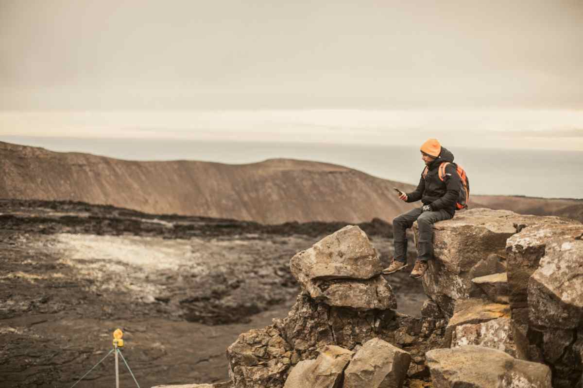 Connectivité solide en Islande Randonneur consultant son téléphone sur des rochers de lave dans un paysage islandais isolé.