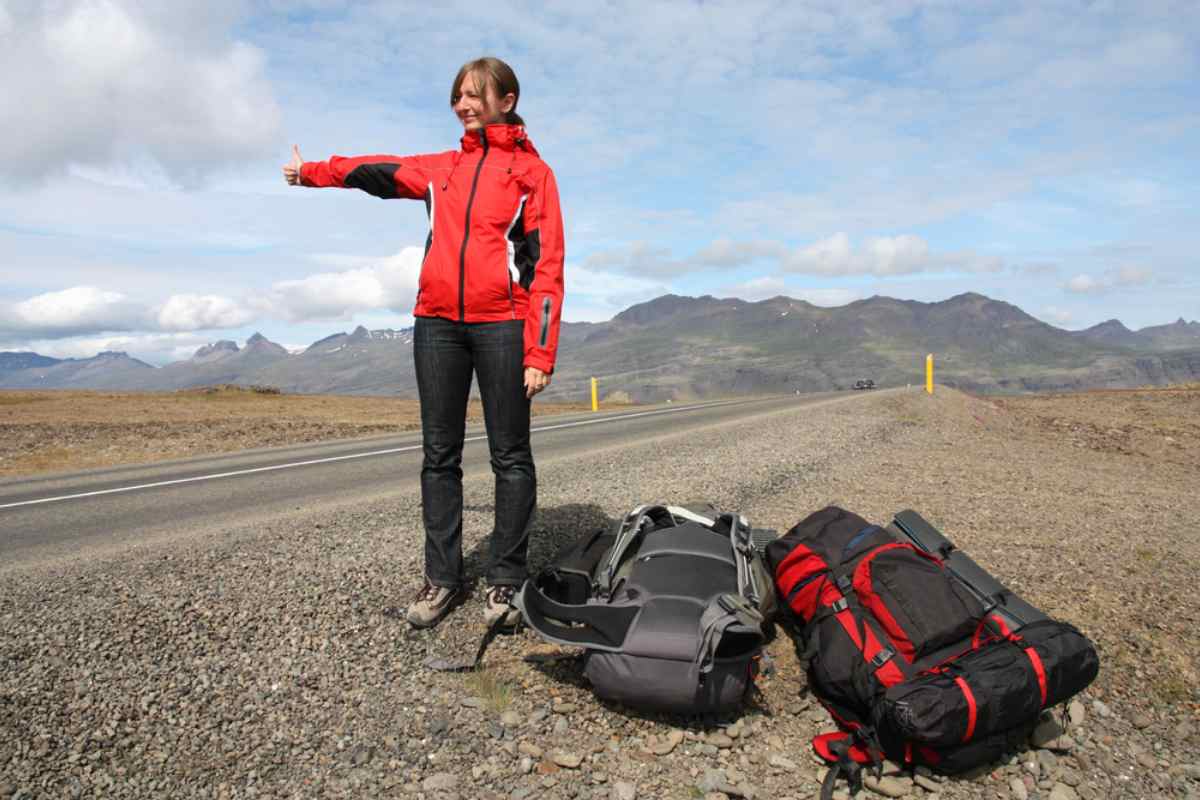 Culture de l’auto-stop en Islande Auto-stoppeuse avec sacs à dos faisant du stop sur une route islandaise.