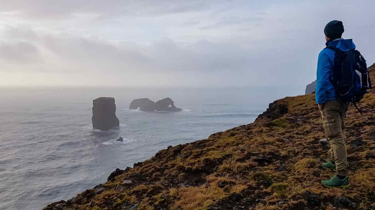 Falaises de Dyrhólaey, Islande Voyageuse contemplant des stacks brumeux depuis les falaises de Dyrhólaey, sud de l’Islande.