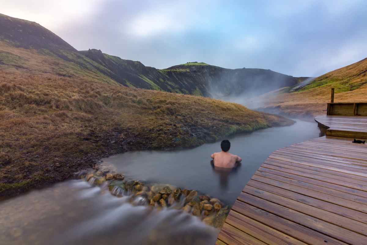 Se détendre dans les sources chaudes islandaises Baignade relaxante dans une rivière d’eau chaude naturelle à côté d’une passerelle en bois.