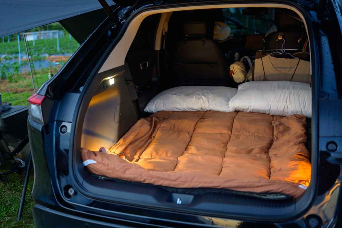 Am&eacute;nagement pour dormir dans le coffre : sac de couchage et oreillers install&eacute;s et &eacute;clair&eacute;s doucement.