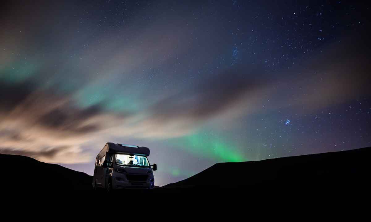 Motorhome gar&eacute; sous un ciel &eacute;toil&eacute; avec de faibles aurores bor&eacute;ales &agrave; l&rsquo;horizon.