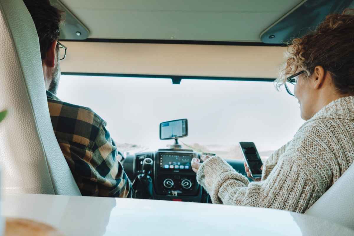Deux voyageurs dans la cabine d&rsquo;un motorhome naviguant avec un t&eacute;l&eacute;phone et un GPS fix&eacute; au tableau de bord.