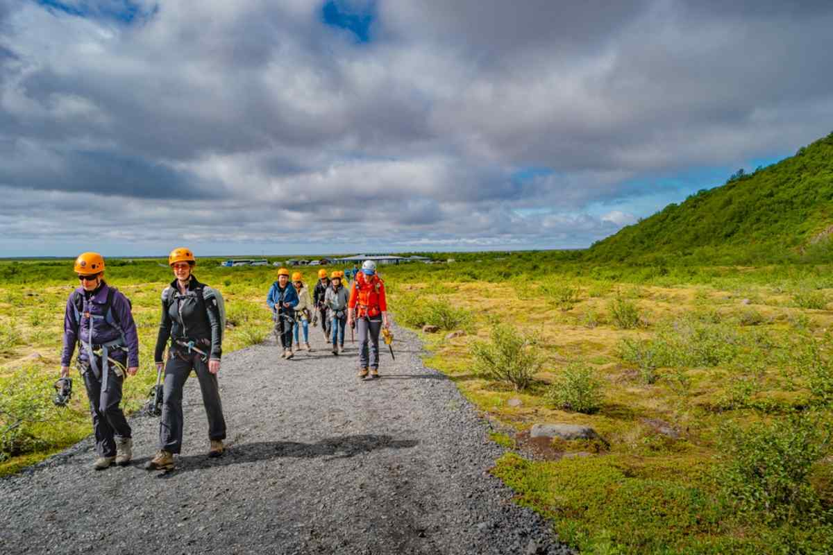 Groupe de randonneurs casqués marchant dans un paysage islandais, entourés de mousse et de ciel d’été.