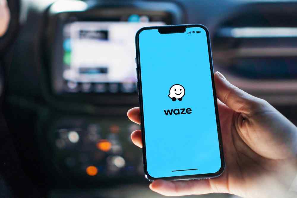 Main tenant un t&eacute;l&eacute;phone avec l&rsquo;application Waze ouverte &agrave; l&rsquo;int&eacute;rieur d&rsquo;une voiture.