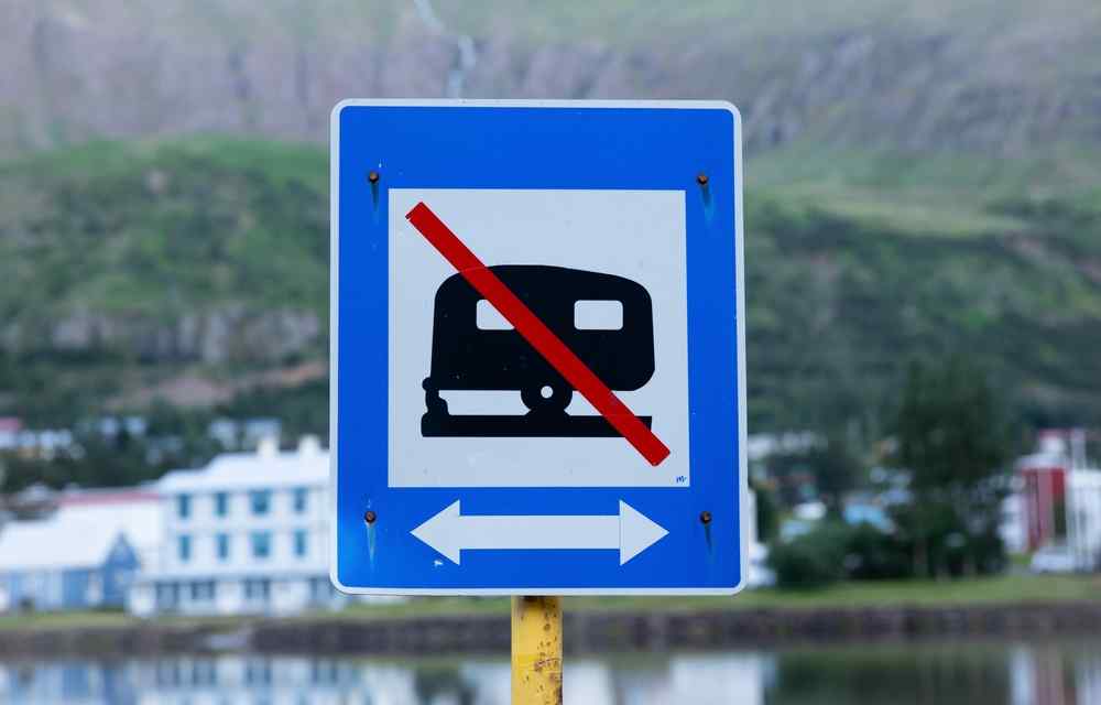 Panneau de stationnement interdit aux camping-cars en Islande avec un village et des montagnes en arri&egrave;re-plan.