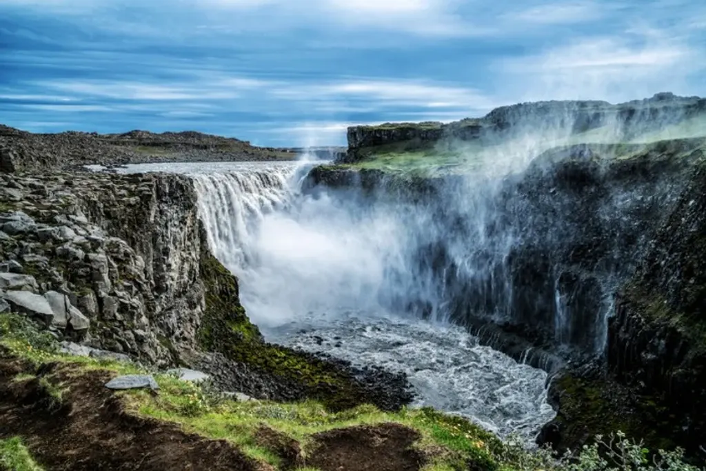Puissante cascade islandaise d&eacute;valant des falaises abruptes, avec de la brume s'&eacute;levant et une v&eacute;g&eacute;tation luxuriante entourant le canyon spectaculaire