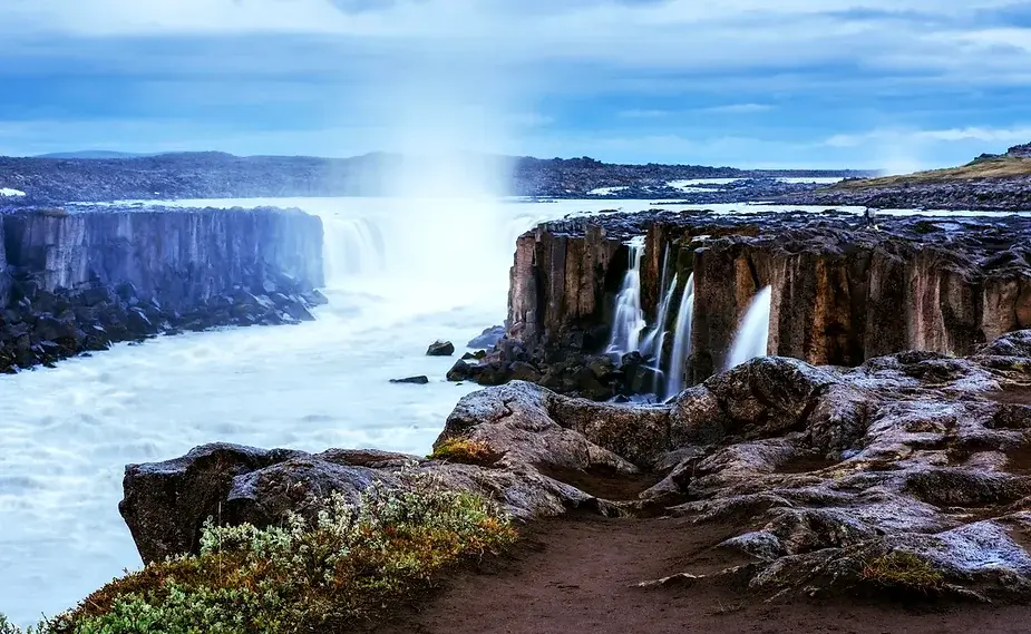 Cascade de Selfoss entourée de falaises de basalte dans le paysage volcanique de l'Islande Cascade de Selfoss coulant sur des falaises de basalte rugueuses dans un paysage volcanique, entourée de terrain rocheux et de verdure, Islande.