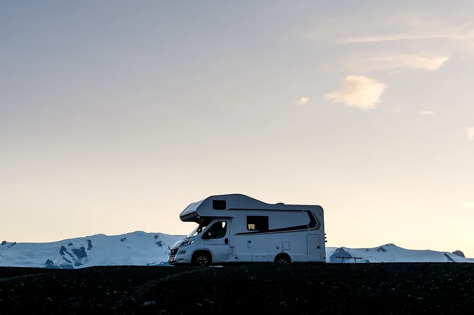 Camping-car au coucher du soleil avec des montagnes enneigées en arrière-plan en Islande Silhouette d'un camping-car garé devant des montagnes enneigées au coucher du soleil en Islande, capturant l'essence de l'aventure et de la liberté.
