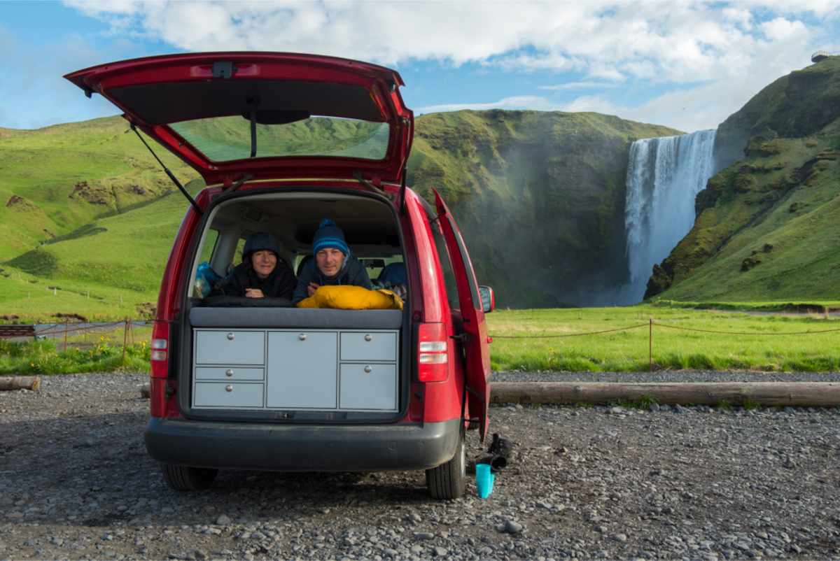 Guidare lungo la Ring Road in camper Turisti sdraiati sul letto della loro campervan davanti alla cascata di Skógafoss