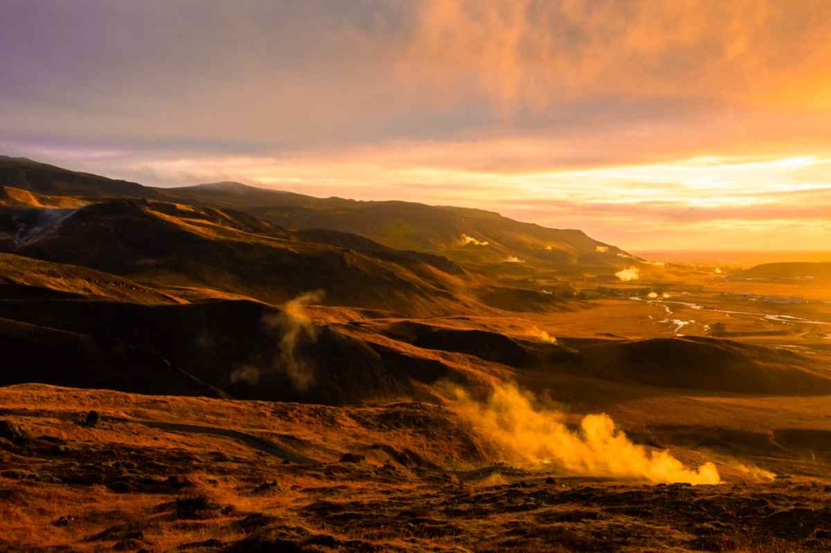 Valle geotermica fumante di Reykjadalur in Islanda illuminata da un tramonto dorato.