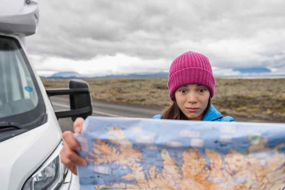 Viaggiatore che tiene una mappa cartacea accanto a un camper su una strada islandese.