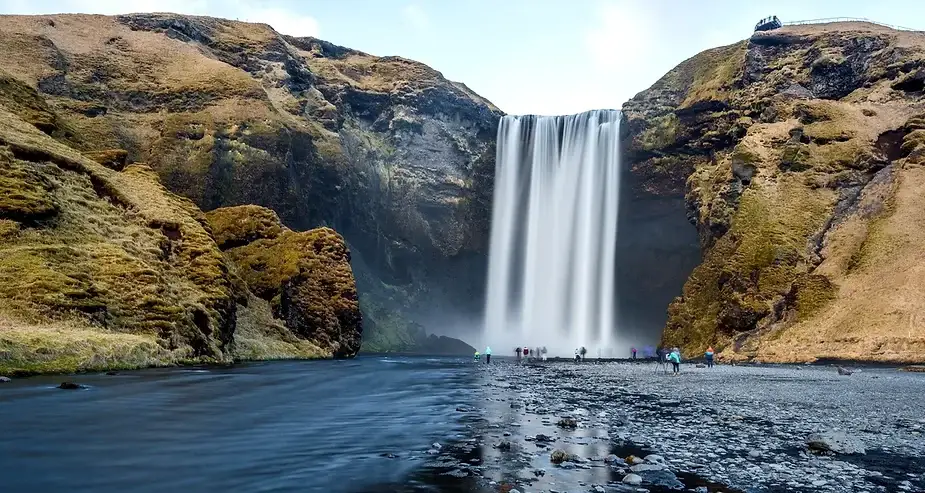 Scopri la maestosa cascata Skógafoss in Islanda: una meraviglia naturale Turisti in piedi vicino alla base della potente cascata Skógafoss in Islanda, con imponenti scogliere e un fiume in primo piano